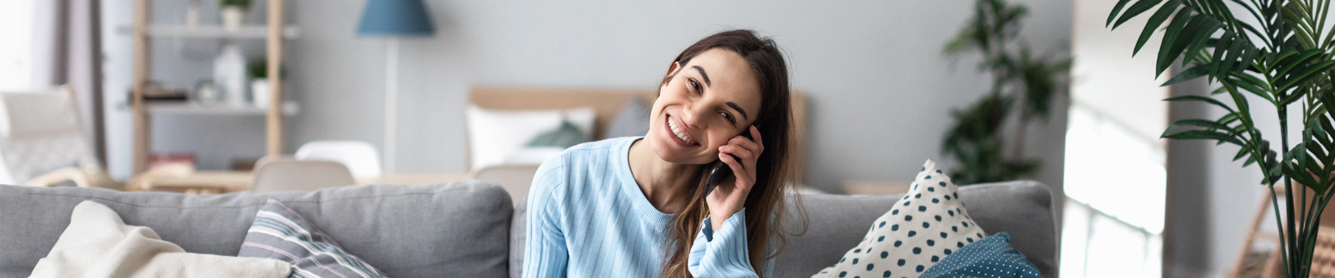 Uśmiechnięta dziewczyna siedzi w pokoju na kanapie i trzyma przy uchu telefon