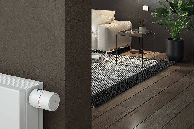 Kobieta relaksująca się na kanapie i sterująca ogrzewaniem za pomocą tabletu.